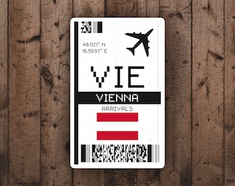 May include: A white sticker with a design resembling a vintage airport luggage tag. The tag features the letters "VIE" for Vienna, Austria, along with the word "ARRIVALS" and the Austrian flag. A silhouette of an airplane is also present.