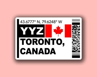 May include: A white sticker featuring the text "YYZ TORONTO, CANADA" with a Canadian flag and coordinates. A barcode is on the right. The background is a pale pink.