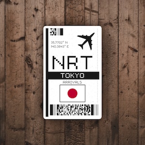May include: A white and black airport arrival sticker with the text "NRT TOKYO ARRIVALS" and a black airplane icon. The sticker also features a red circle on a white background, representing the Japanese flag.