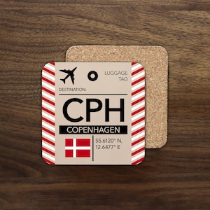 May include: A square coaster with a luggage tag design for Copenhagen. The coaster features the letters "CPH", the destination name, and the Danish flag. The border has red and white diagonal stripes. A second, cork coaster is behind it.