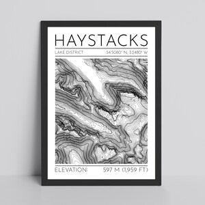 May include: Black framed print with a topographic map of Haystacks in the Lake District. The print includes the text "HAYSTACKS" and "LAKE DISTRICT". Elevation is listed as 597 m. The map is in black and white.