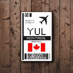 May include: A white airport arrival tag with black text and a black airplane icon. The tag reads "YUL MONTREAL ARRIVALS" and includes the coordinates "45.4657° N 73.7455° W". A Canadian flag is displayed in the center of the tag.