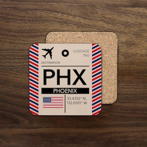 May include: A square cork coaster featuring a luggage tag design with a beige background, red and blue striped borders, and a black airplane icon. It displays the text LUGGAGE TAG, DESTINATION, PHX, PHOENIX, the US flag, and coordinates.