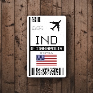 May include: A white airport arrival sign with black text and a black airplane icon. The sign reads "IND" and "INDIANAPOLIS" with the coordinates "39.7205° N 86.2937° W". The sign also has a barcode and an American flag.