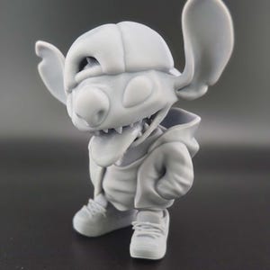 May include: A gray figurine of a cartoon character, wearing a backward baseball cap, hoodie, and sneakers. The character has large ears, a wide mouth with visible teeth, and is in a crouching pose. The figurine is detailed and appears to be 3D-printed.