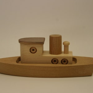 May include: A wooden toy boat with a brown roof, a chimney, and three round portholes. The boat is made of light wood and has a simple design.