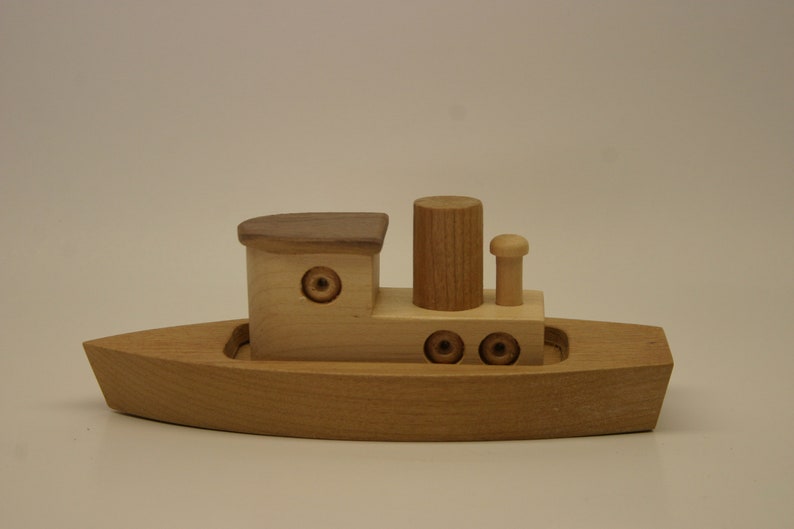 May include: A wooden toy boat with a brown roof, a chimney, and three round portholes. The boat is made of light wood and has a simple design.