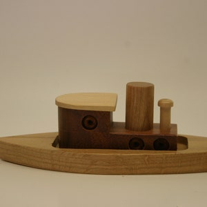 May include: A wooden toy tugboat with a brown hull, a light brown deck, and a light brown smokestack. The tugboat has two round portholes on each side.