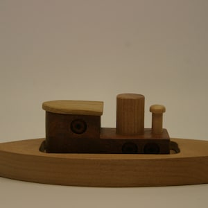 May include: A wooden toy boat with a brown cabin and a light brown deck. The boat has a small smokestack and a mast with a flag.