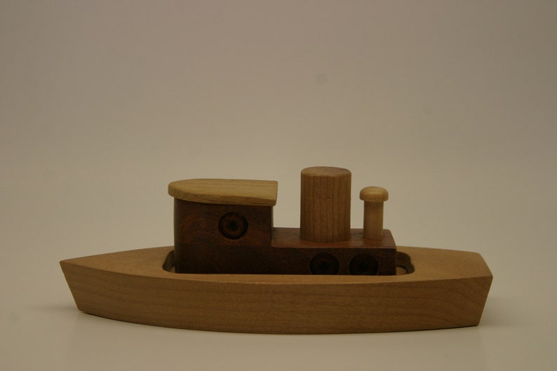 May include: A wooden toy boat with a brown cabin and a light brown deck. The boat has a small smokestack and a mast with a flag.