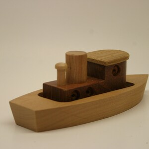 May include: A wooden toy boat with a brown and natural wood cabin and a single smokestack. The boat is made of light wood and has a simple design.