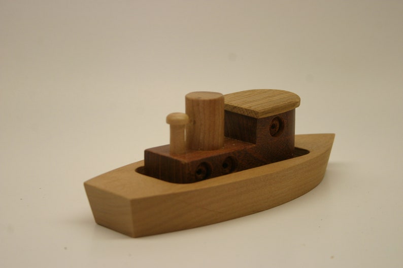 May include: A wooden toy boat with a brown and natural wood cabin and a single smokestack. The boat is made of light wood and has a simple design.