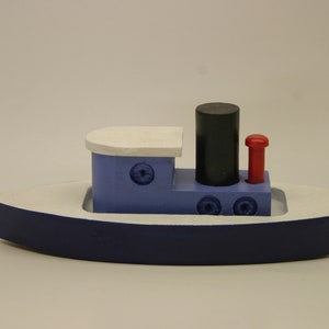 May include: A blue and white wooden toy tugboat with a black smokestack and a red flag. The boat has a white deck and a blue hull.