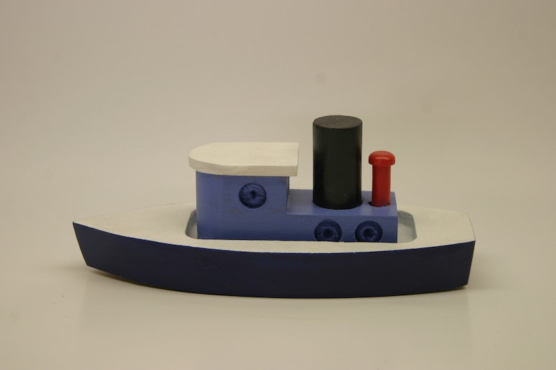 May include: A blue and white wooden toy tugboat with a black smokestack and a red flag. The boat has a white deck and a blue hull.