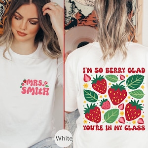 May include: White t-shirt with the text "MRS. SMITH" in pink with strawberries on the front and a white t-shirt with the text "I'M SO BERRY GLAD YOU'RE IN MY CLASS" in pink with strawberries on the back.
