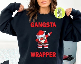 Pode incluir: Camisola de cor preta com um Pai Natal vermelho e branco a fazer dab e o texto "Gangsta Wrapper".
