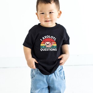 Pode incluir: Uma camiseta preta com um gr&aacute;fico de p&ocirc;r do sol retr&ocirc; com um axolotl e o texto "I axolotl questions".