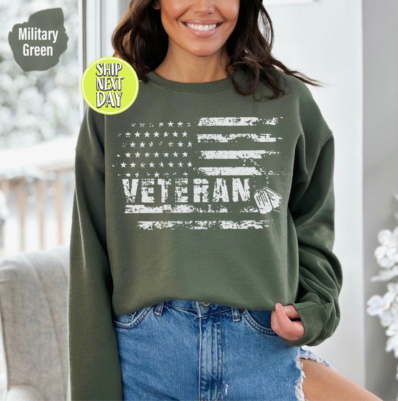 Peut inclure: Un sweat-shirt vert avec un motif de drapeau am&eacute;ricain blanc d&eacute;lav&eacute; et le mot "Veteran" avec des m&eacute;dailles militaires.