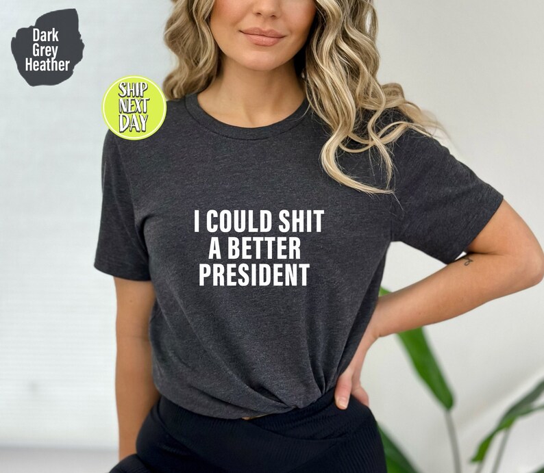 May include: Dark grey heather t-shirt with the text "I could shit a better president" printed in white.
