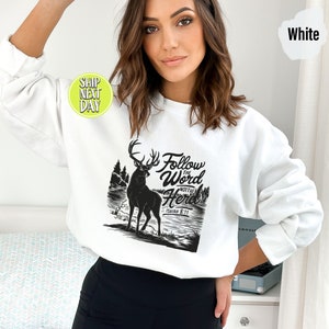 May include: White sweatshirt with a black graphic of a deer, trees, and the text "Follow the Word Not the Herd" and "Isaiah 8:11". The sweatshirt is a crew neck style.