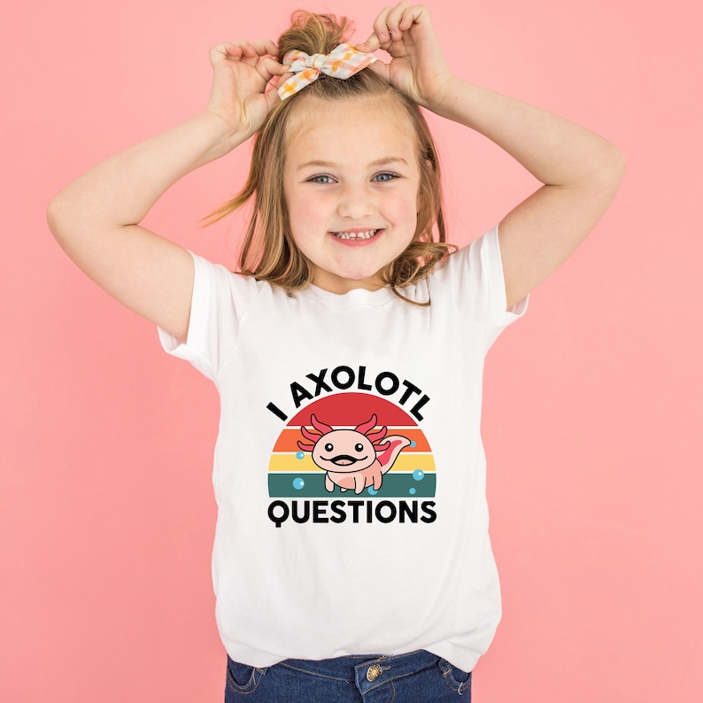 Pode incluir: Camiseta branca com um gr&aacute;fico retro de um axolotl com o texto "I axolotl questions".