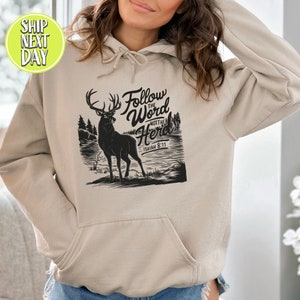 May include: A beige hoodie with a front pocket and a drawstring hood. The front features a black graphic of a deer with the text "Follow the Word Not the Herd" and "Isaiah 8:11".