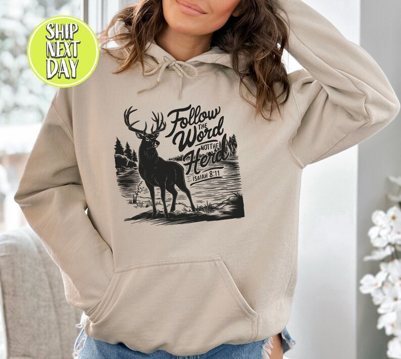 May include: A beige hoodie with a front pocket and a drawstring hood. The front features a black graphic of a deer with the text "Follow the Word Not the Herd" and "Isaiah 8:11".