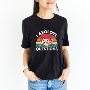 Pode incluir: Camiseta preta com um gr&aacute;fico retro de um axolotl com o texto "I axolotl questions".