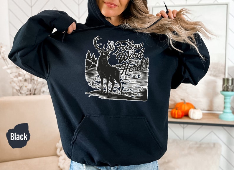 May include: Black hoodie with a white graphic of a deer in a forest scene. Text on the hoodie reads "Follow the Word Not the Herd" and "Isaiah 8:19". The hoodie has a front pocket and a hood with a drawstring.