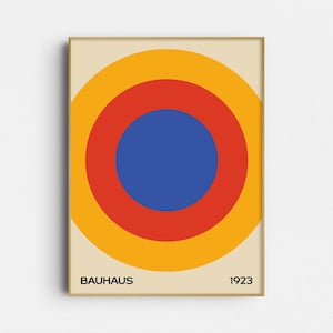 May include: A framed rectangular wall art print featuring a series of three concentric circles in yellow, red, and blue against a cream background. The text "BAUHAUS" is printed in black in the bottom left corner and "1923" in the bottom right corner.