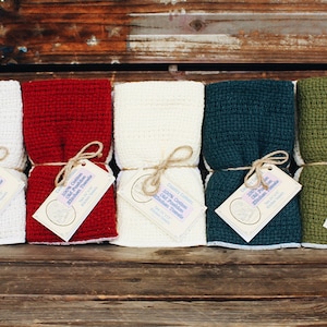May include: Ten kitchen towels in various colors, including light blue, gray, white, red, cream, teal, green, orange, and white. The towels are folded and tied with twine, with a small tag attached to each.