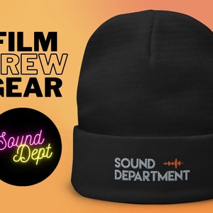 Op de afbeelding: Zwarte beanie met de woorden "SOUND DEPARTMENT" in wit geborduurd, met een oranje golfvormige afbeelding. De woorden "FILM CREW GEAR" staan boven een zwarte cirkel met de woorden "Sound Dept" in neonroze en geel.
