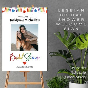 May include: A white sign on an easel with the text "Welcome to Jacklyn & Michelle's" and "Bridal Shower" in rainbow colors. The sign also includes a photo of two women and the date August 25th, 2026. The words "Lesbian Bridal Shower Welcome Sign" are also displayed.