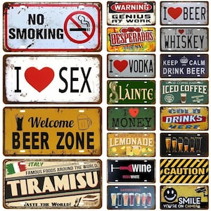 Könnte beinhalten: Eine Sammlung von Metallschildern im Vintage-Stil mit verschiedenen Designs und Texten. Schilder sind u.a. "No Smoking", "I Love Whiskey", "Welcome Beer Zone", "Tiramisu" und "Smile You're on Camera". Die Schilder haben ein gealtertes Aussehen.