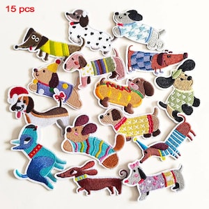 May include: A set of 15 embroidered dog patches in various colours and designs. The patches feature different breeds of dogs wearing sweaters, hats, and other accessories. The patches are on a white background.