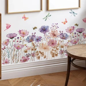 May include: A wall decal depicting a watercolour floral design with pink, purple, and peach flowers, butterflies, bees, and dragonflies. The design is applied to a white wall, creating a nature-inspired aesthetic.