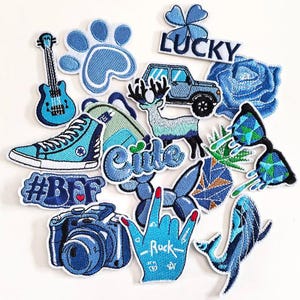 May include: A collection of blue embroidered patches with various designs, including a guitar, paw print, high-top sneaker, car, deer, rose, and a camera. Some patches have text like "Cute", "#BFF", "Lucky", and "Rock".
