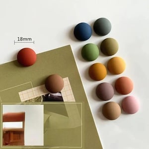 Puede incluir: Una colección de imanes redondos y coloridos, cada uno de aproximadamente 18 mm de diámetro, dispuestos sobre una superficie blanca y un papel verde. Los imanes vienen en varios colores, incluyendo rojo, azul, verde y marrón. La imagen muestra el tamaño de los imanes.