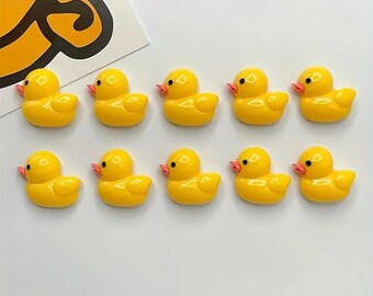 Puede incluir: Diez pequeñas figuras de patos amarillos con picos naranjas están dispuestas en dos filas sobre una superficie blanca. Los patos miran en la misma dirección. Una porción de un gráfico amarillo y negro es visible en la esquina superior izquierda.