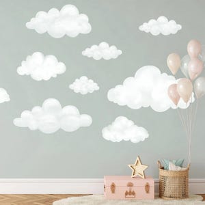 May include: A set of white cloud wall decals arranged on a light green wall. To the right, a cluster of light pink and white balloons is tied to a woven basket containing pillows. A pink storage trunk with a gold star ornament sits on the floor.