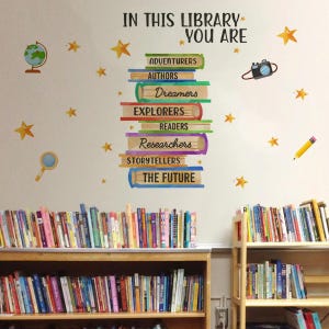 May include: A library scene with bookshelves filled with books. The wall features a decorative design with the text "IN THIS LIBRARY YOU ARE" and stacked books labeled with words like "Adventurers" and "Authors". Yellow stars and other illustrations are scattered around.
