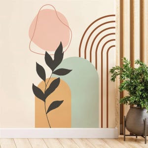 May include: Abstract wall art featuring a minimalist design with geometric shapes and a botanical element. The artwork includes a dark gray leaf branch, a pink irregular shape, and a brown arch design against a beige background. The wall art is displayed above a white baseboard.