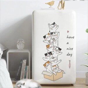 May include: A white refrigerator with a cartoon illustration of several cats stacked on top of each other. The cats have various markings and are in a playful pose. The text "have a nice day" is written on the side.