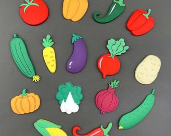 May include: A collection of colorful, cartoon-style vegetable magnets, including a red tomato, yellow bell pepper, green chili pepper, and red bell pepper. Other vegetables include a cucumber, carrot, eggplant, radish, potato, pumpkin, lettuce, red onion, corn, and red chili pepper.