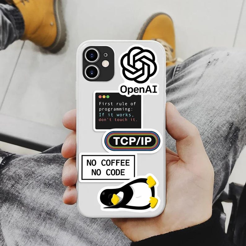 Op de afbeelding: Een witte smartphonehoesje versierd met stickers met een technisch thema. De stickers bevatten het OpenAI-logo, "TCP/IP" en de tekst "First rule of programming: If it works, don't touch it." Een pingu&iuml;nsticker en "NO COFFEE NO CODE" zijn ook zichtbaar.