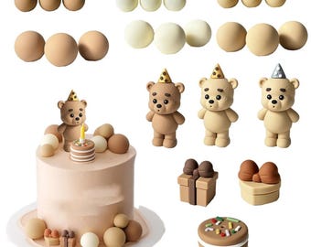 May include: A cake decorating set featuring a light pink cake topped with a bear figurine, a miniature cake, and various spheres. Includes three bear figurines with party hats, additional spheres in beige and white, two gift boxes, and a cookie.