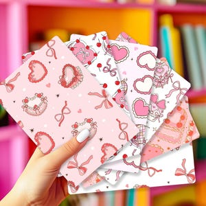 May include: A set of six pink and white patterned paper sheets with hearts, bows, and cherries. The sheets are designed for scrapbooking, card making, or other paper crafts.