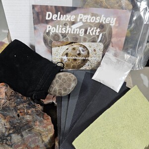 May include: A Deluxe Petoskey Polishing Kit includes a black velvet pouch, a Petoskey stone, sandpaper, a polishing cloth, and a packet of polishing compound. The kit is designed for polishing Petoskey stones. The kit's packaging features the text "Deluxe Petoskey Polishing Kit".