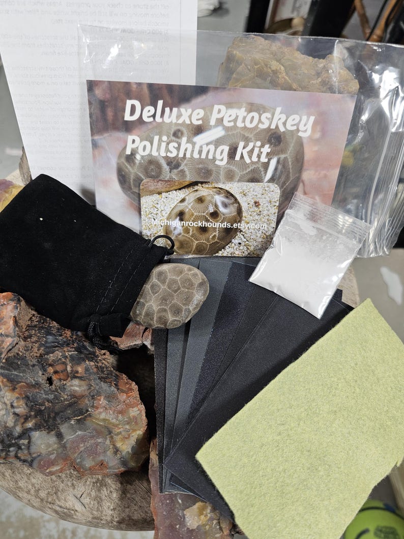 May include: A Deluxe Petoskey Polishing Kit includes a black velvet pouch, a Petoskey stone, sandpaper, a polishing cloth, and a packet of polishing compound. The kit is designed for polishing Petoskey stones. The kit's packaging features the text "Deluxe Petoskey Polishing Kit".