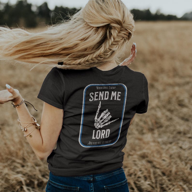Puede incluir: Camiseta negra con un gr&aacute;fico blanco y azul en la espalda. El gr&aacute;fico presenta una mano de esqueleto haciendo un gesto con la mano, con las palabras "SEND ME LORD" y "WHOM SHALL I SEND? AND WHO WILL GO FOR US?" en un marco rectangular.
